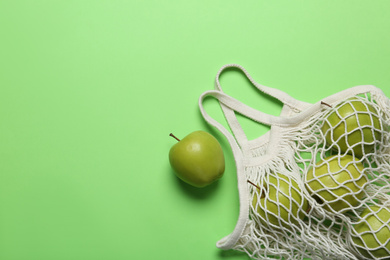 Net bag with juicy apples on green background, flat lay. Space for text