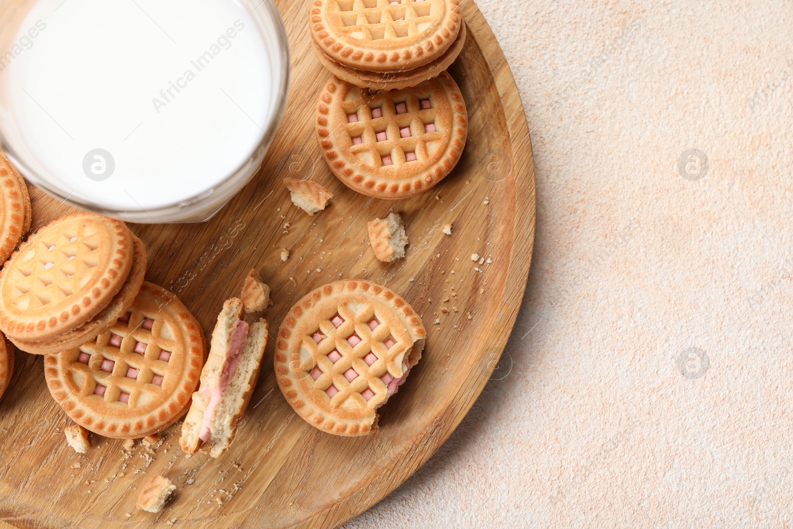 Photo of Tasty sandwich cookies with cream and glass of milk on beige background, top view. Space for text