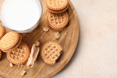 Tasty sandwich cookies with cream and glass of milk on beige background, top view. Space for text