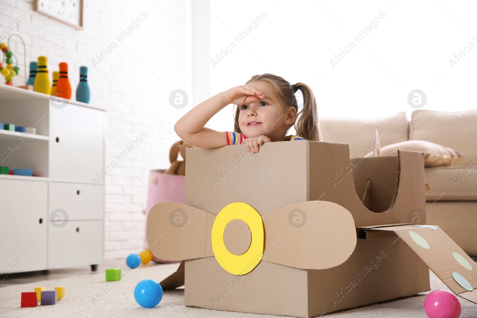 Photo of Cute little child playing with cardboard plane at home