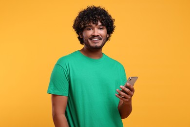 Photo of Handsome smiling man using smartphone on yellow background