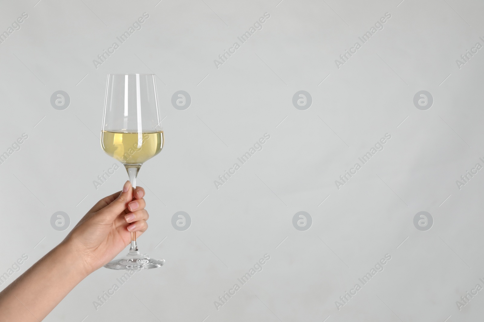 Photo of Woman holding glass of white wine on light background, closeup. Space for text