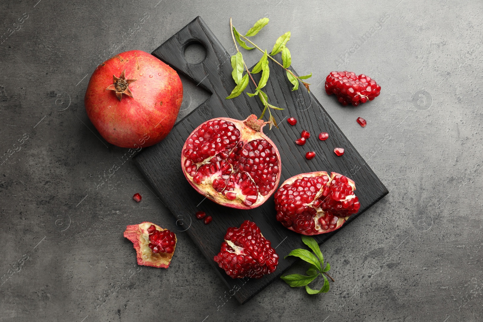 Photo of Fresh pomegranates and green leaves on grey table, top view