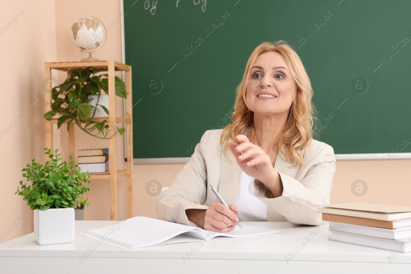 Photo of Professor giving lecture near green board at desk in classroom