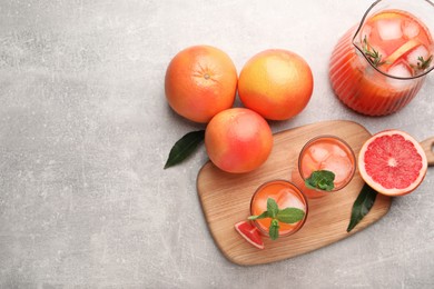 Photo of Tasty freshly made grapefruit juice, fruits and mint on light grey table, flat lay. Space for text