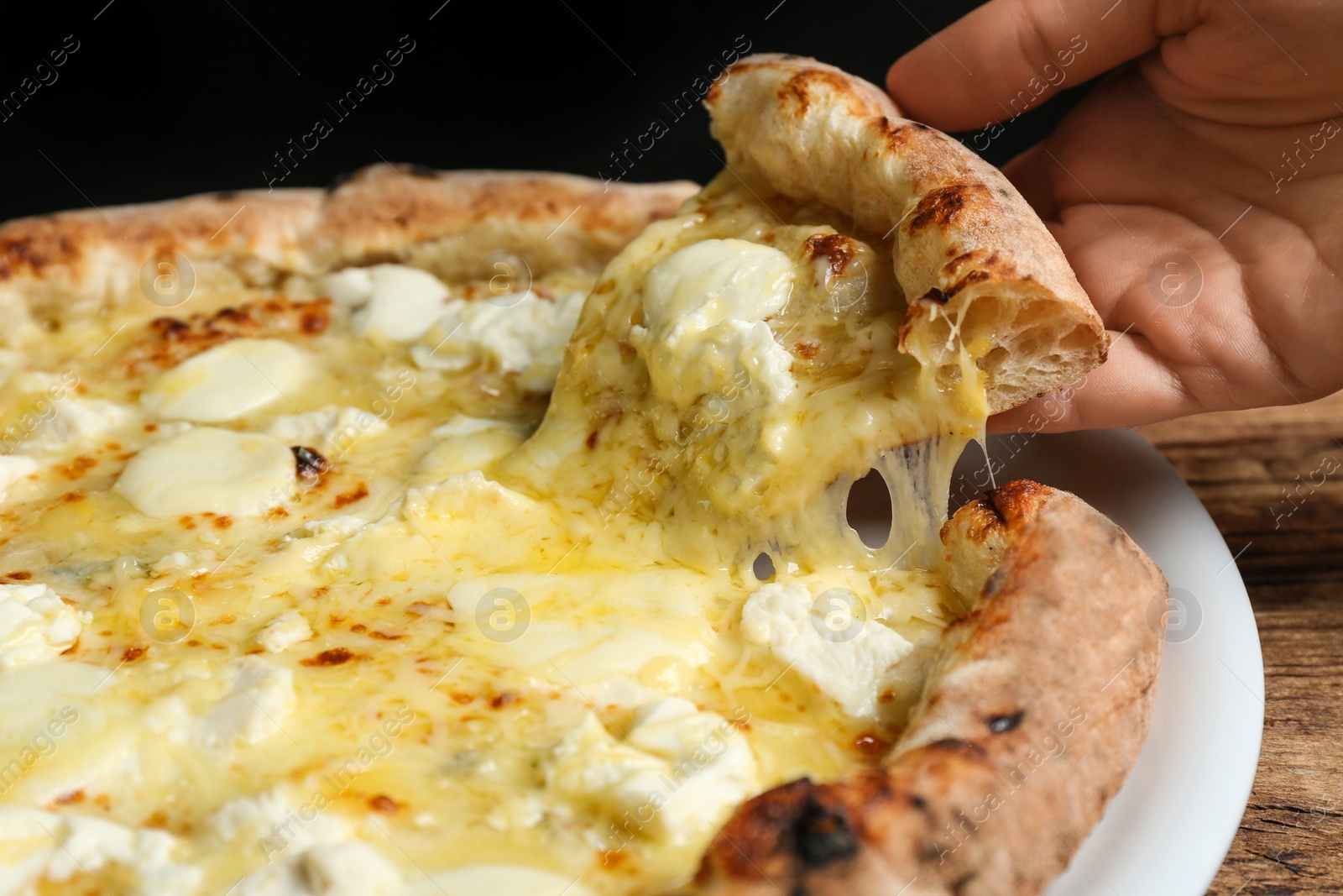 Photo of Woman taking slice of tasty cheese pizza at wooden table, closeup