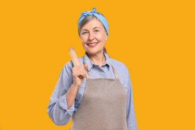 Happy housewife with rolling pin on orange background