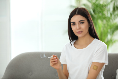 Young woman with nicotine patch and cigarette at home. Space for text