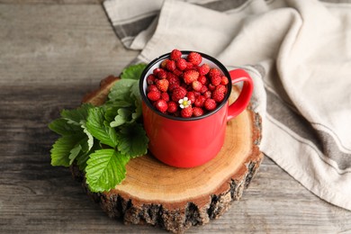 Photo of Fresh wild strawberries in mug and leaves on wooden table
