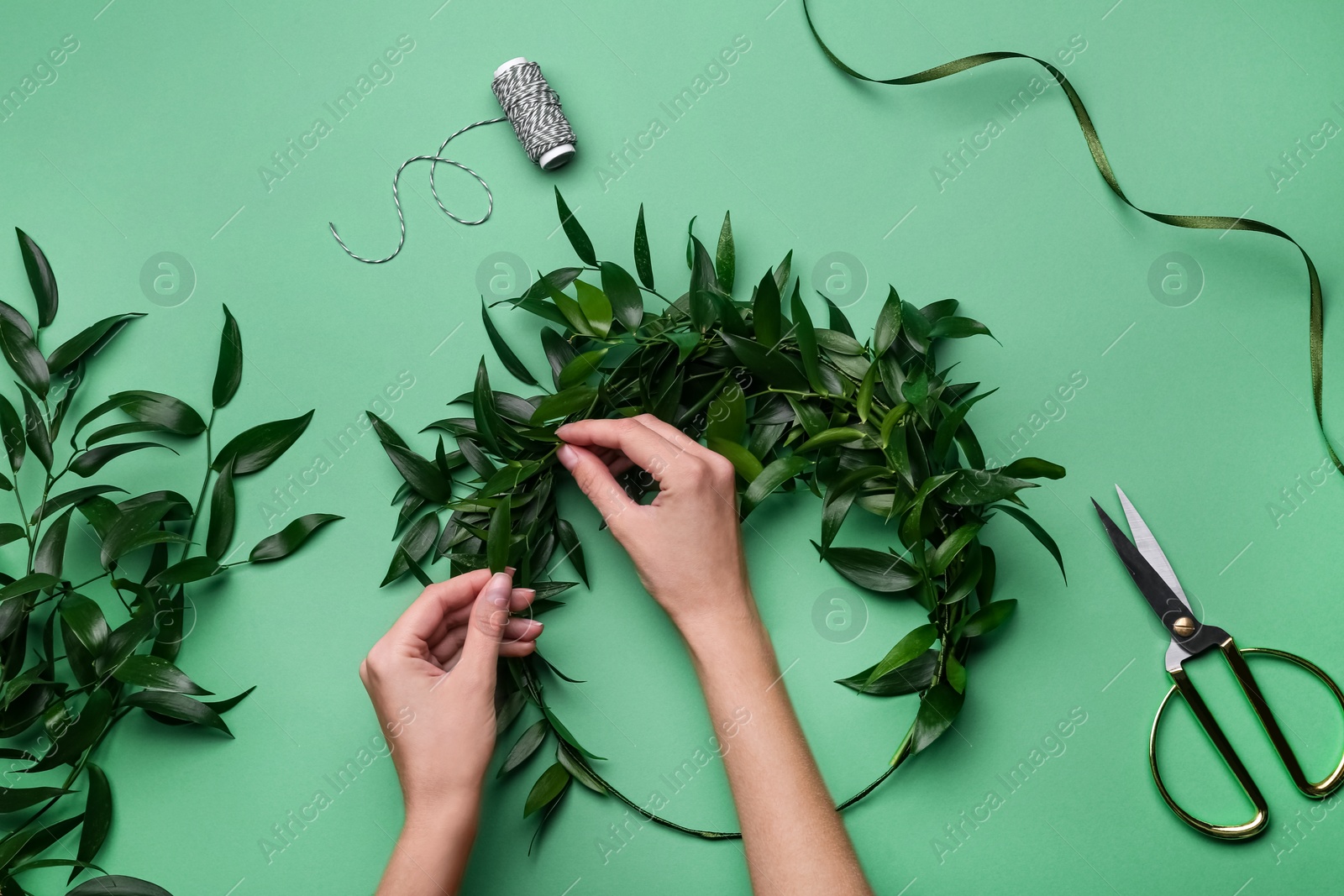 Photo of Florist making beautiful mistletoe wreath on green background, top view. Traditional Christmas decor