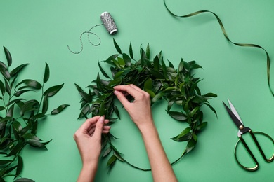 Photo of Florist making beautiful mistletoe wreath on green background, top view. Traditional Christmas decor