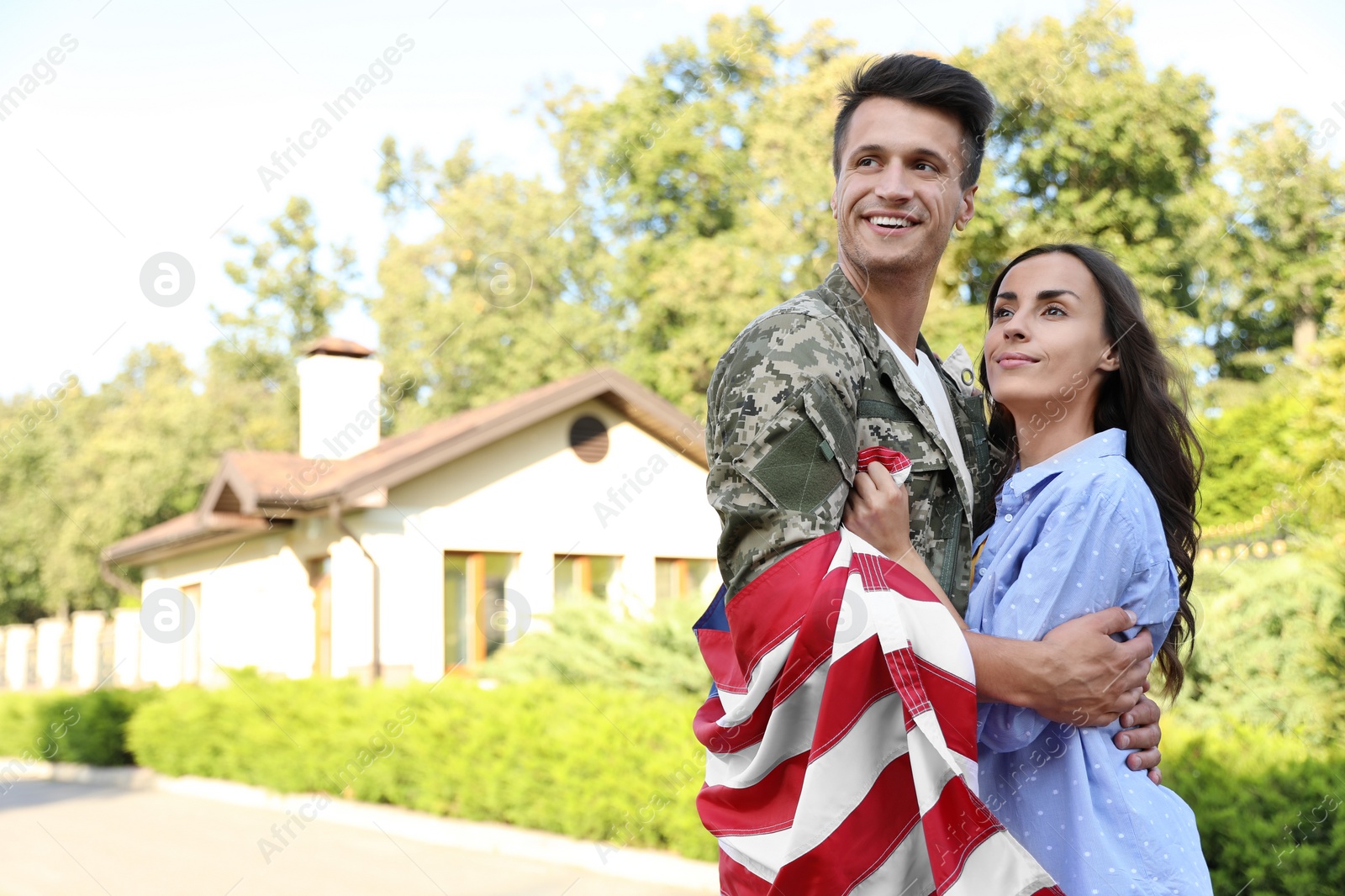 Photo of Man in military uniform with American flag hugging his wife outdoors