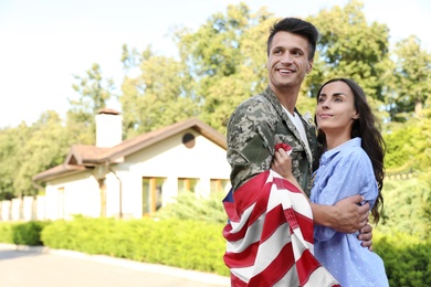 Man in military uniform with American flag hugging his wife outdoors