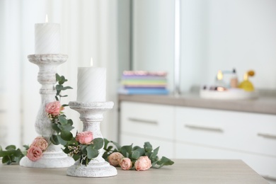Photo of Vintage candlesticks with burning candles, roses and eucalyptus on table in room. Space for text