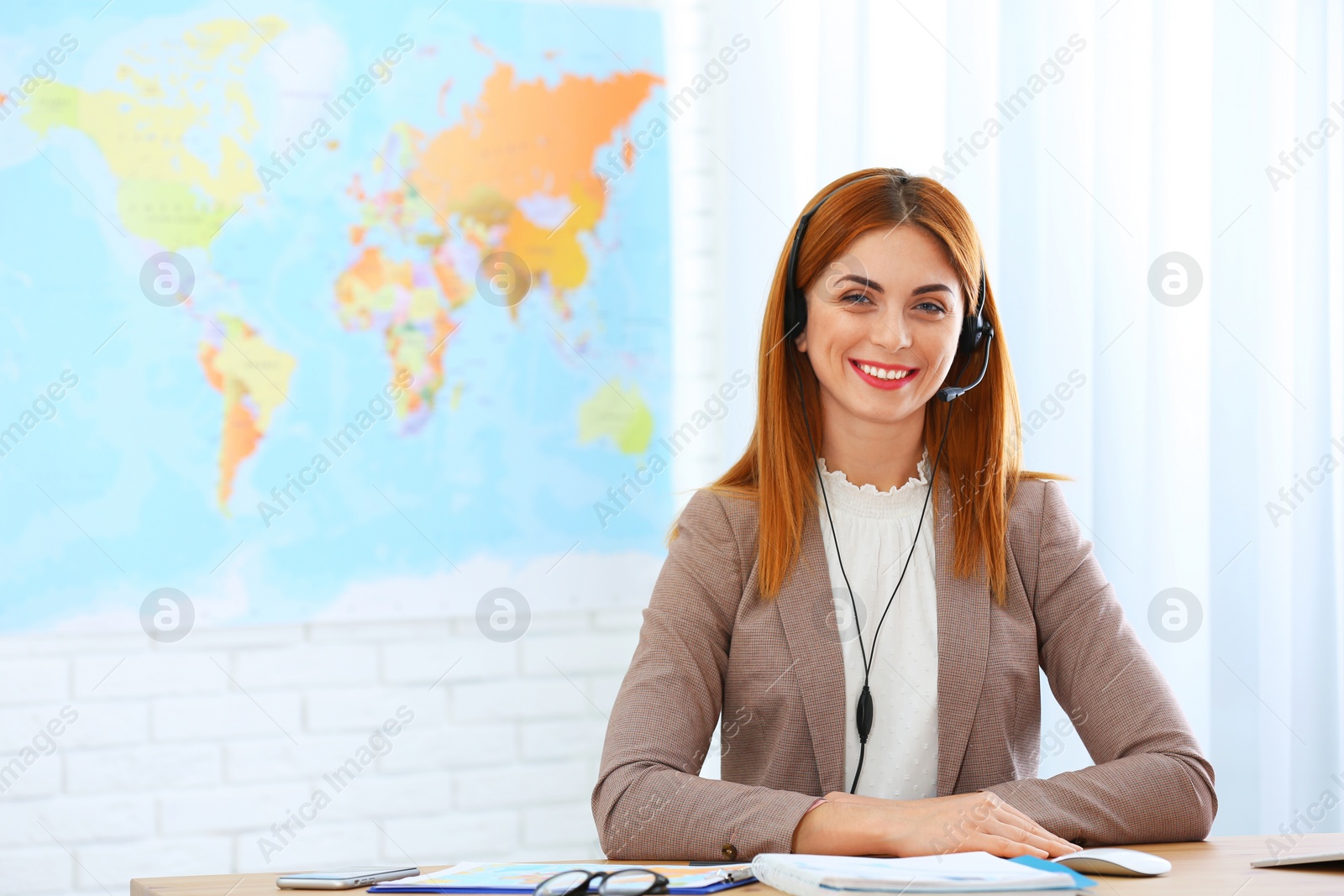 Photo of Beautiful consultant with headset sitting at table in travel agency. Space for text