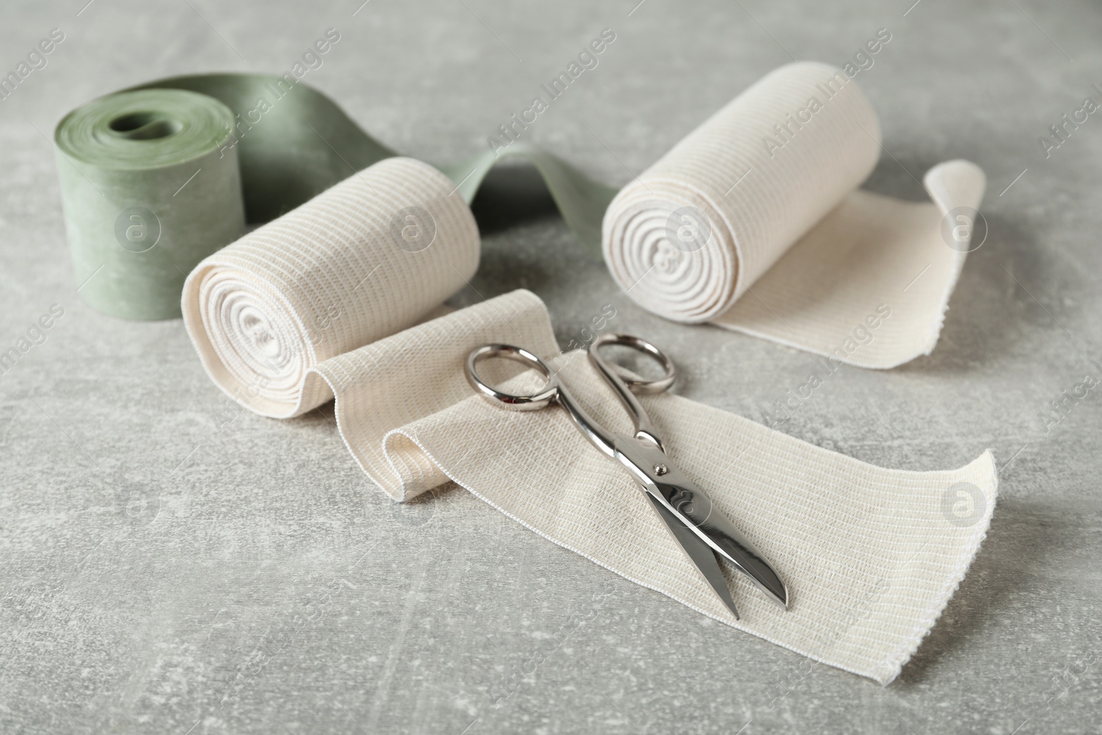 Photo of Medical bandage rolls and scissors on grey table