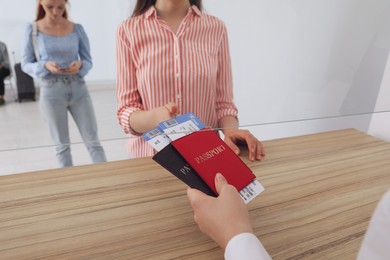 Agent giving passports with tickets to client at check-in desk in airport, closeup