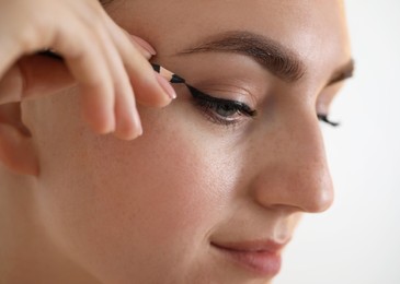 Photo of Makeup product. Woman applying black eyeliner on blurred background, closeup