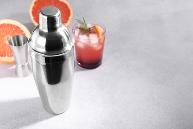 Photo of Metal shaker, delicious cocktail, jigger and grapefruit on light grey table, space for text