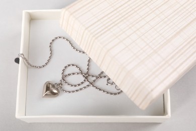 Photo of Metal chain with pendant in box on light table, top view. Luxury jewelry