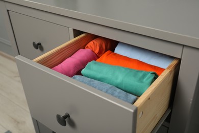 Different rolled shirts in drawer indoors. Organizing clothes