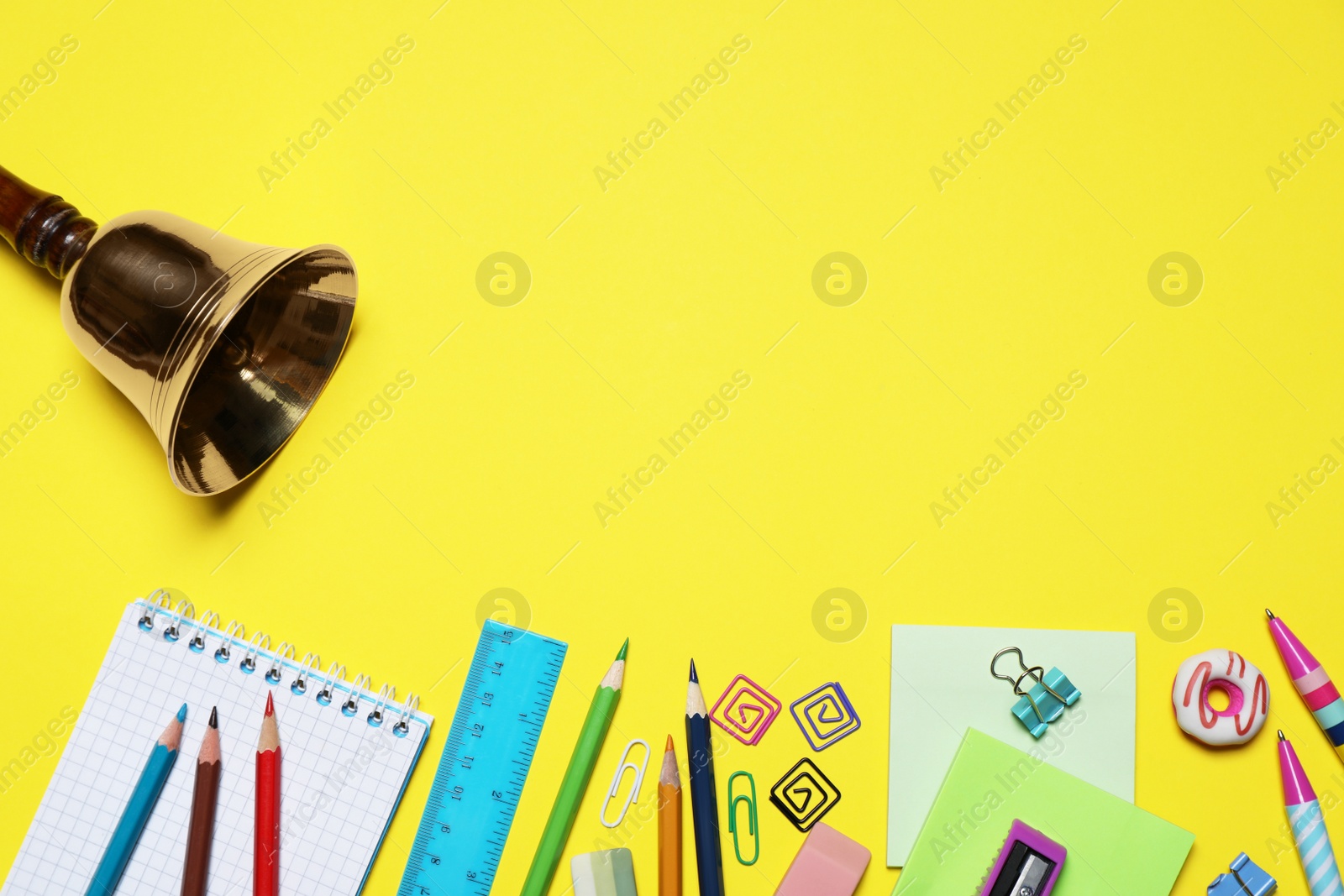 Photo of Different stationery and school bell on yellow background, flat lay. Space for text