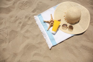 Photo of Tube of sunscreen, starfish and beach accessories on sand, top view with space for text. Sun protection care