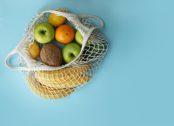 Photo of Net bag with fruits on light blue background, top view. Space for text