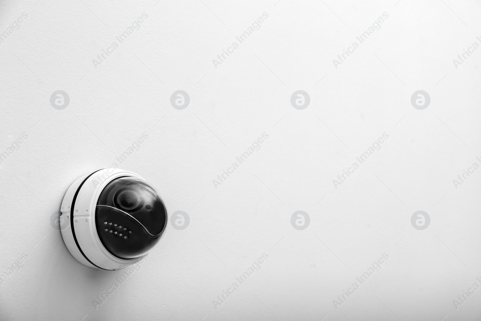 Photo of Modern CCTV security camera on white wall. Space for text