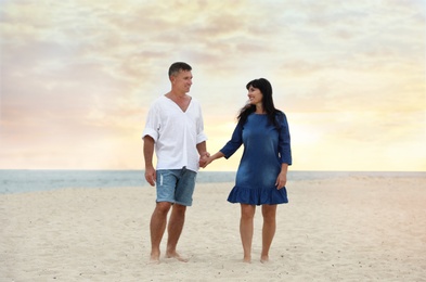 Happy mature couple walking together on sea beach at sunset