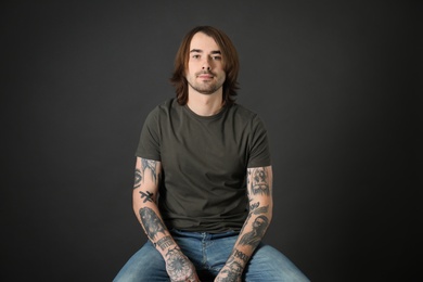 Photo of Young man with tattoos on arms against black background