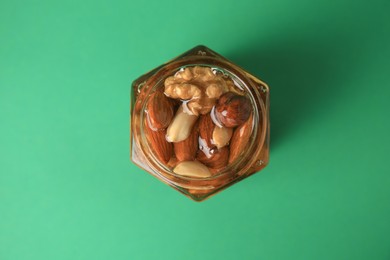 Photo of Jar with different tasty nuts and honey on green background, top view