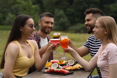 Photo of Happy friends clinking glasses with cocktails at table outdoors