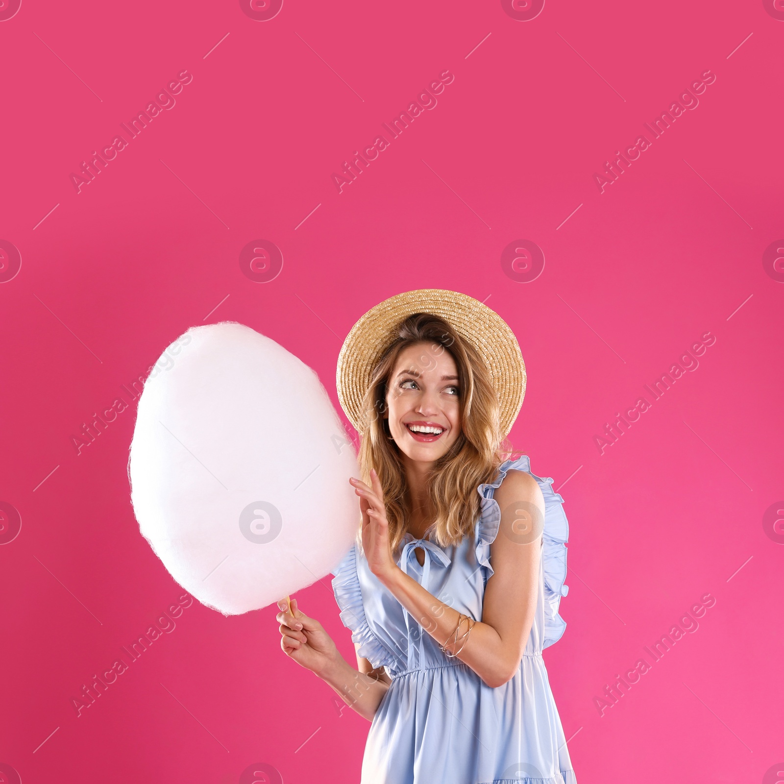 Photo of Happy young woman with cotton candy on pink background