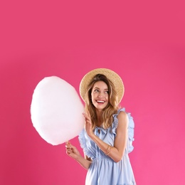 Photo of Happy young woman with cotton candy on pink background