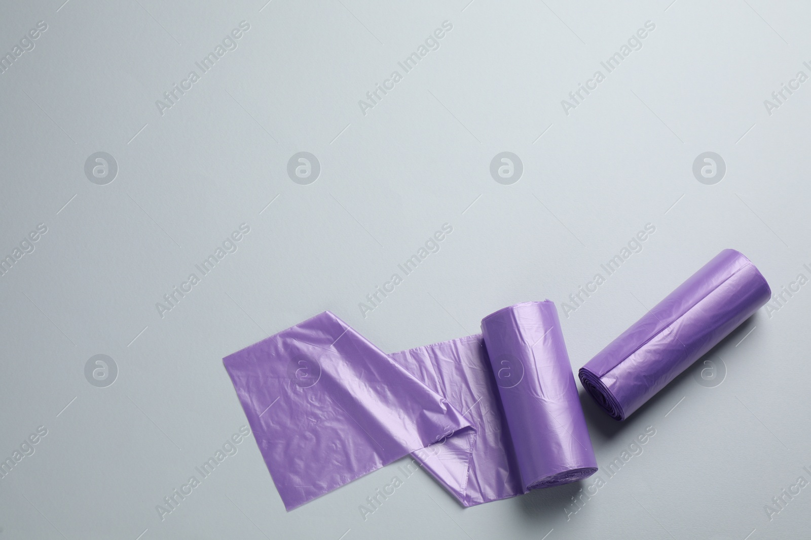 Photo of Rolls of violet garbage bags on light grey background, flat lay. Space for text