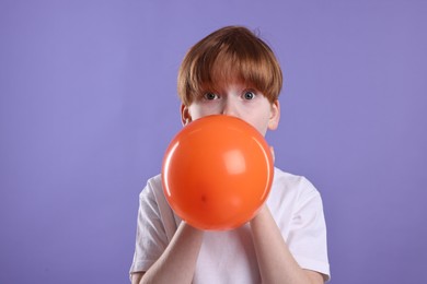 Photo of Boy inflating orange balloon on violet background