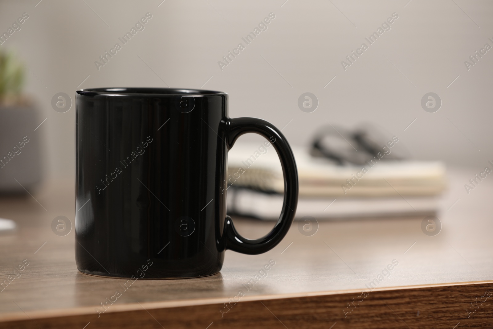 Photo of Black ceramic mug on wooden table at workplace. Space for text