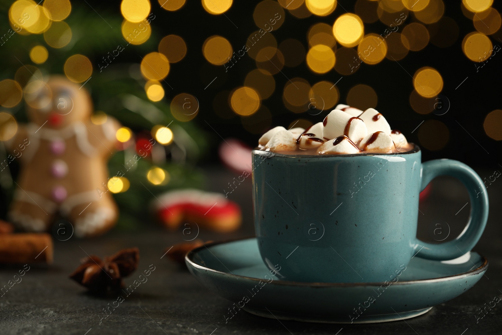 Photo of Delicious hot chocolate with marshmallows and syrup on black table against blurred lights, closeup. Space for text