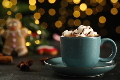 Delicious hot chocolate with marshmallows and syrup on black table against blurred lights, closeup. Space for text