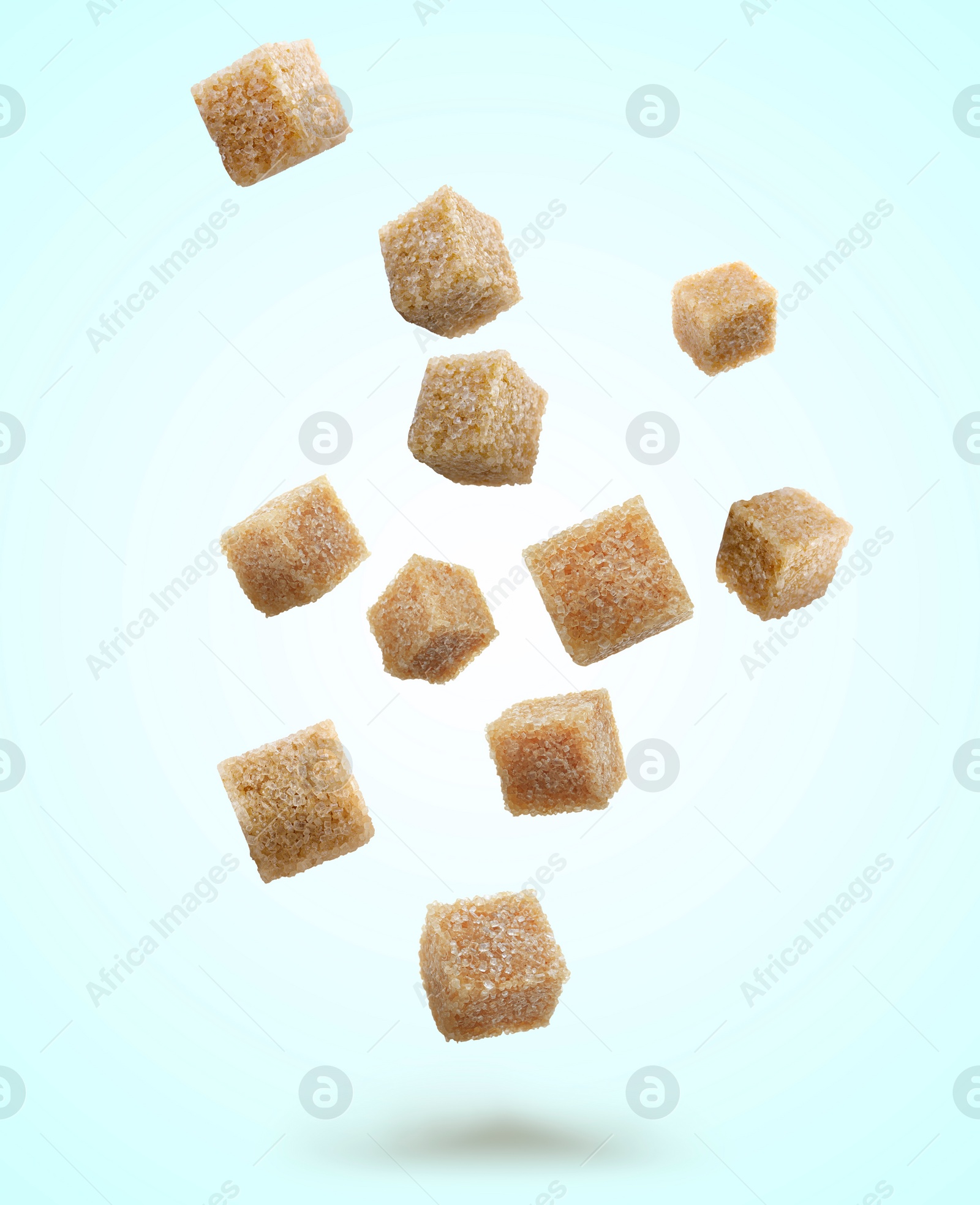 Image of Brown cane sugar cubes falling on light blue background