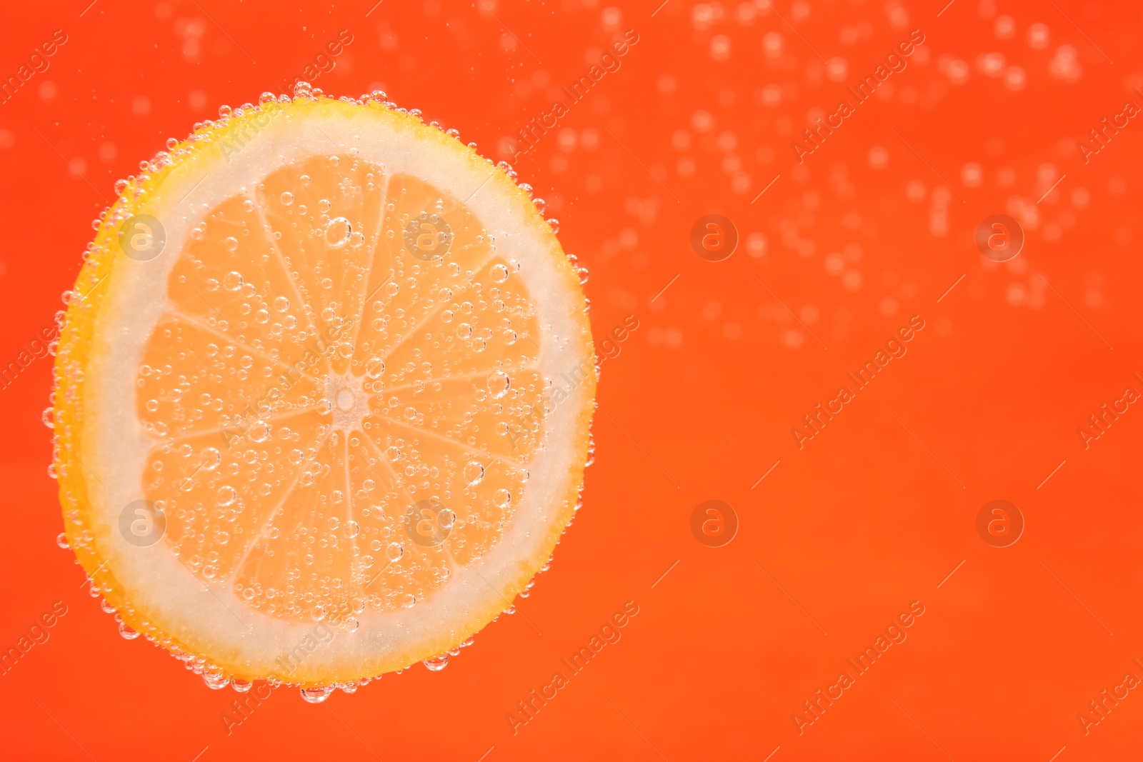 Photo of Slice of lemon in sparkling water on orange background, space for text. Citrus soda