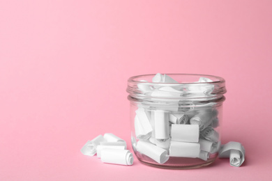 Photo of Glass jar full of rolled paper sheets on pink background, space for text
