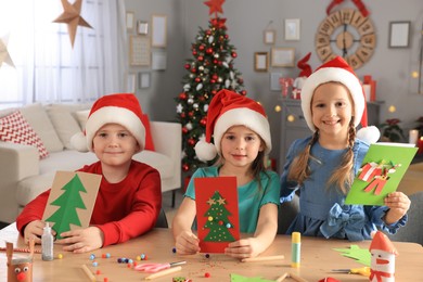 Cute little children in Santa hats making beautiful Christmas greeting cards at home