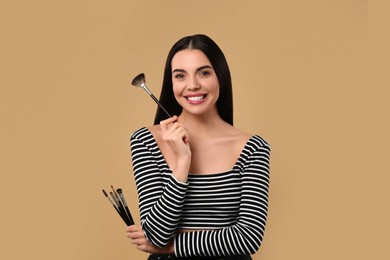 Photo of Happy woman with different makeup brushes on light brown background, space for text