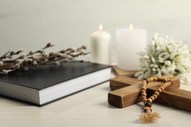 Photo of Wooden cross, rosary beads, Bible, church candles and snowdrops on white table