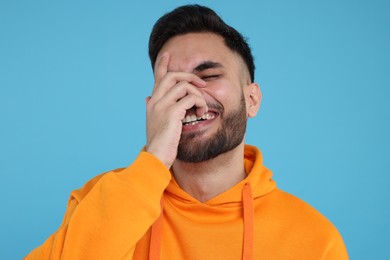 Handsome young man laughing on light blue background