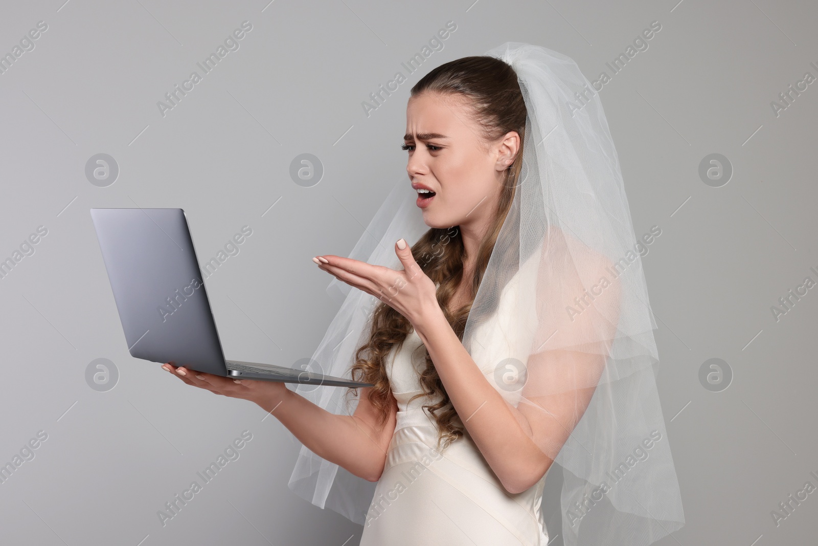 Photo of Shocked bride with laptop on gray background