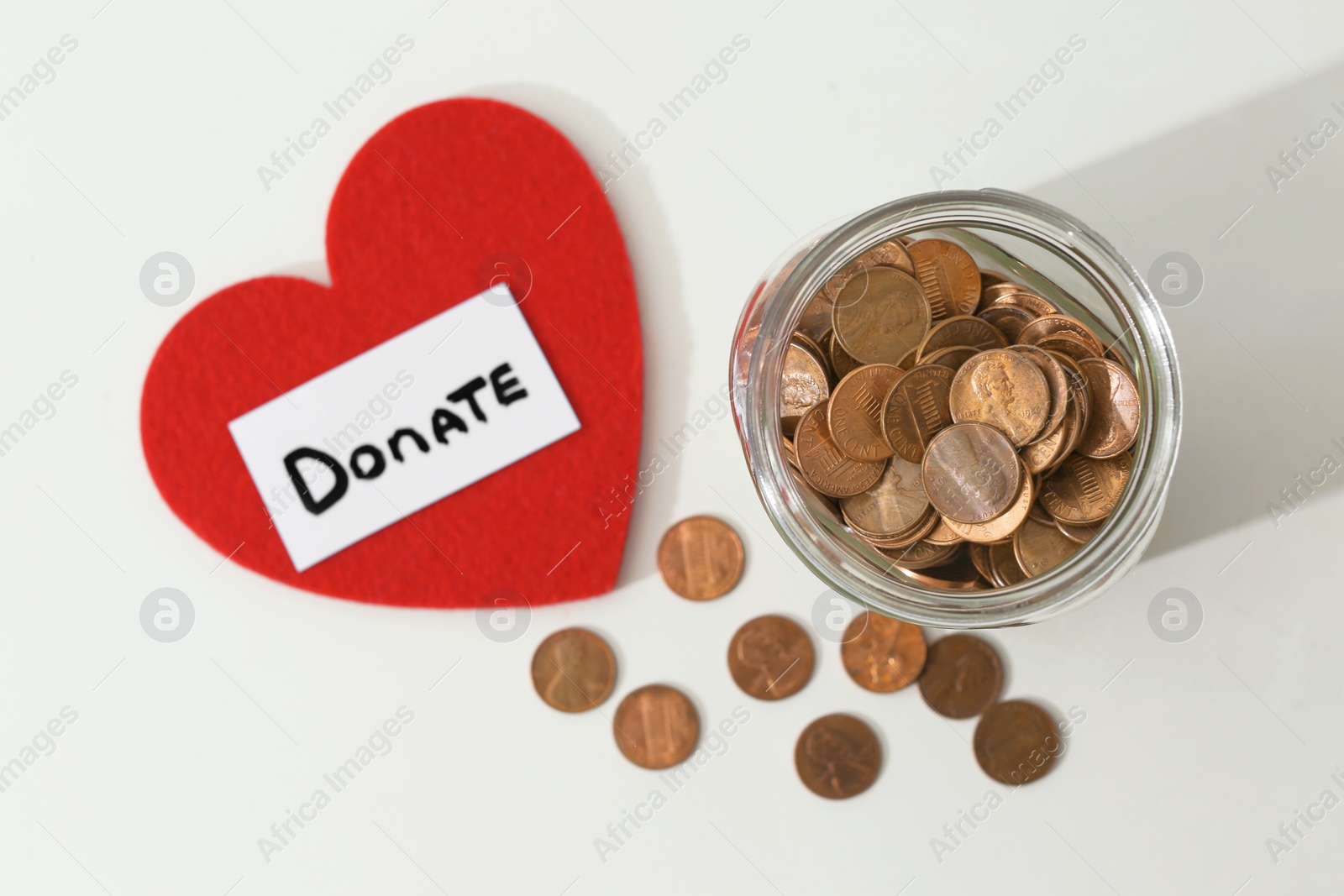 Photo of Donation jar, coins and red heart on white background, top view