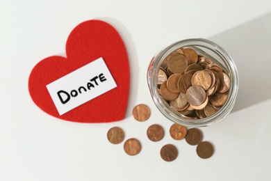 Photo of Donation jar, coins and red heart on white background, top view